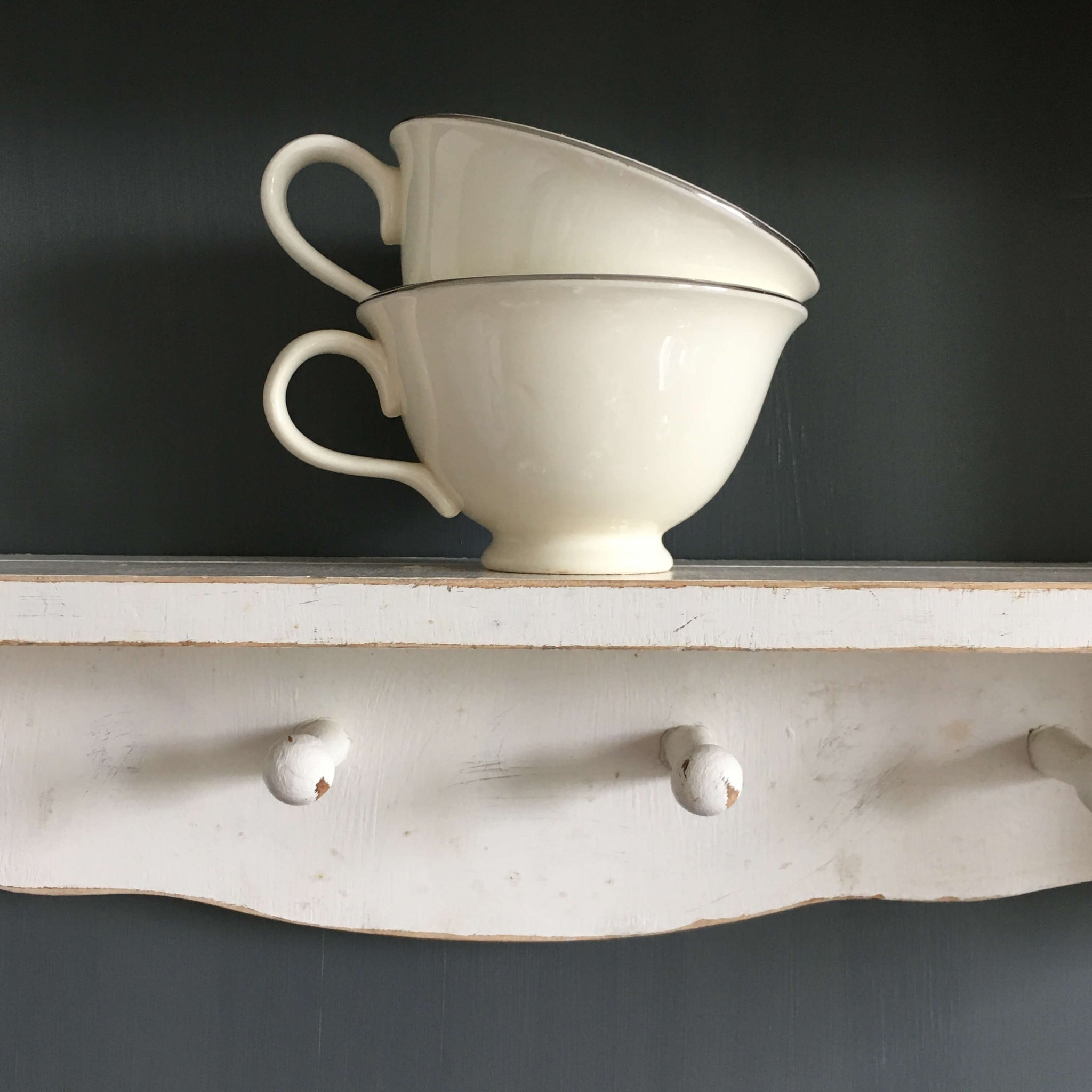 two vintage white teacups on a wooden shelf
